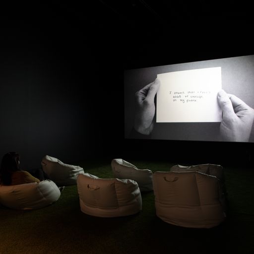 Screenshot from the artist installation featuring a projected image of a note with numerous bags on the ground 